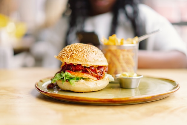 Jonge vrouw met afrohaar die een smakelijke klassieke hamburger met frietjes eten