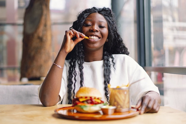 Jonge vrouw met afrohaar die een smakelijke klassieke hamburger met frietjes eten