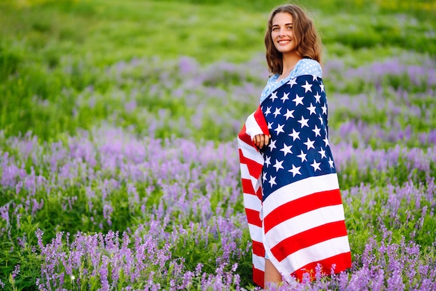 Jonge vrouw met Amerikaanse vlag van de VS op bloeiende weide Onafhankelijkheidsdag 4 juli