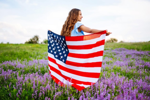 Jonge vrouw met Amerikaanse vlag van de VS op bloeiende weide Onafhankelijkheidsdag 4 juli