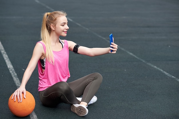 Jonge vrouw met basketbal met behulp van telefoon na de training, selfie maken.