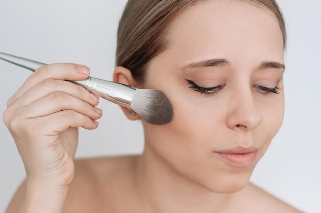 Foto jonge vrouw met behulp van een borstel die blozen op de huid aanbrengt een meisje dat make-up doet cosmetisch schoonheidsconcept