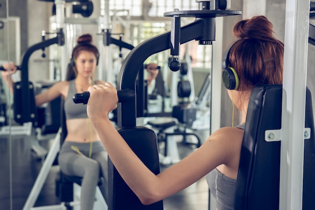 Jonge vrouw met behulp van gewichtheffen apparatuur om een enorme borst en arm op indoor sport gym te bouwen.