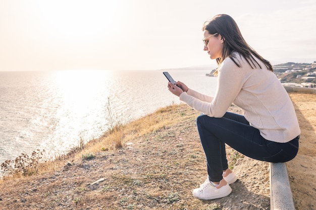 Jonge vrouw met behulp van haar mobiele telefoon in de voorkant van de zee in het voorjaar