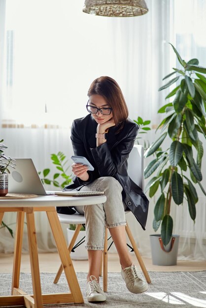 Jonge vrouw met behulp van laptop en mobiele telefoon zittend op de werkplek thuis werken op afstand