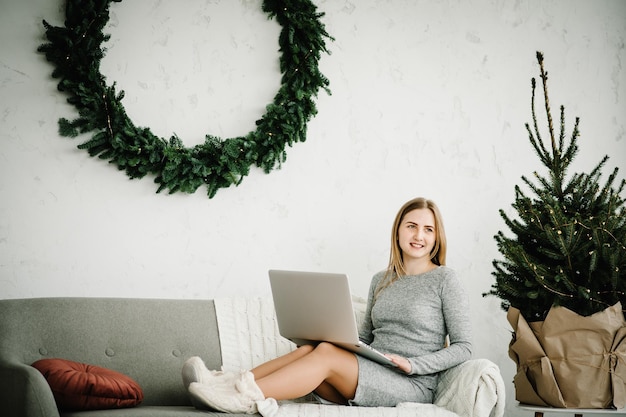 Jonge vrouw met behulp van laptop en werken thuis kantoor in de buurt van versierde dennenboom met kerst interieur Kerst verkoop Meisje typen op laptop in huis Xmas concept Vakantie plannen Zoeken op het web