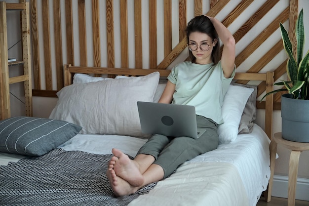 Jonge vrouw met behulp van laptop typen liggend op het bed werken op afstand thuis werken