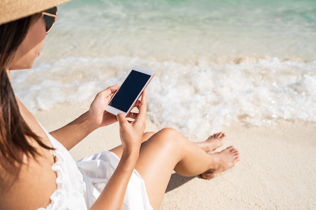 Jonge vrouw met behulp van mobiele telefoon op het strand zittend bij de golven