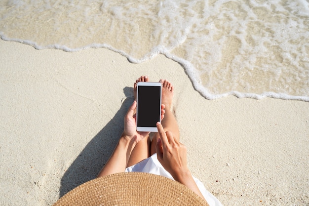 Jonge vrouw met behulp van mobiele telefoon op prachtig tropisch wit zandstrand met golfschuim en transparante zee, zomervakantie en reisconcept met kopieerruimte