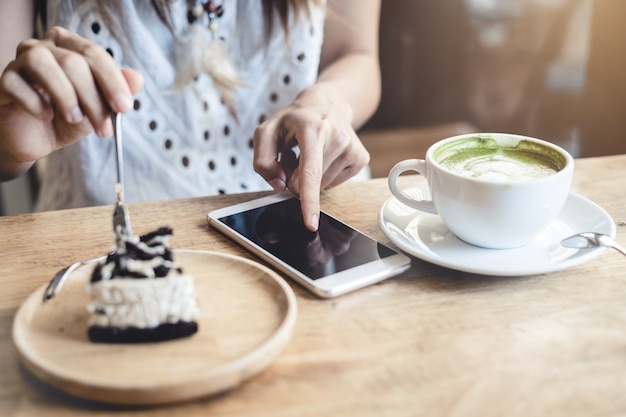 Jonge vrouw met behulp van slimme telefoon en het eten van taart