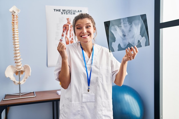 Jonge vrouw met bekkenradiografie schreeuwend trots, overwinning en succes vierend erg opgewonden met opgeheven armen