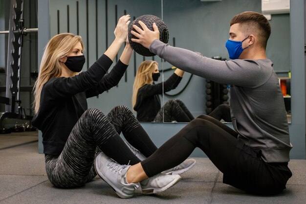 Jonge vrouw met beschermend masker traint met personal trainer in de sportschool tijdens de Covid-19 pandemie. Ze pompt haar spieren op met een halter. Zachte focus