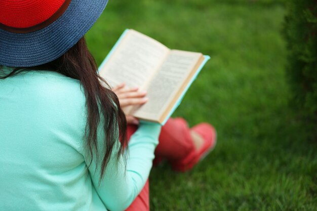 Jonge vrouw met boek zittend op groen gras buitenshuis