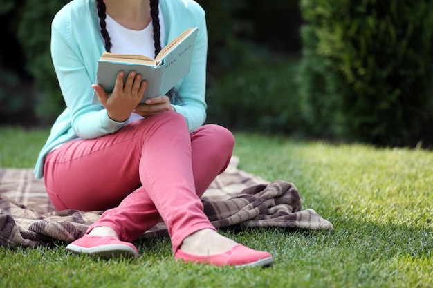 Jonge vrouw met boek zittend op groen gras buitenshuis