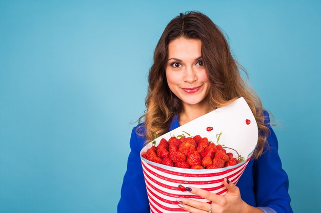 Jonge vrouw met boeket aardbeien op blauwe achtergrond