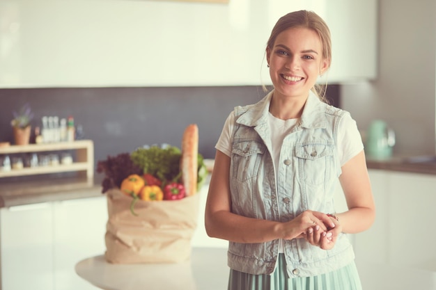 Jonge vrouw met boodschappentas met groenten die in de keuken staan