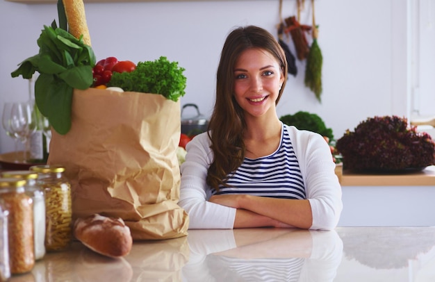 Jonge vrouw met boodschappentas met groenten die in de keuken staan