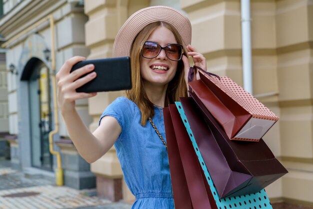Jonge vrouw met boodschappentassen selfie wandelen in een stad op zomerdag maken
