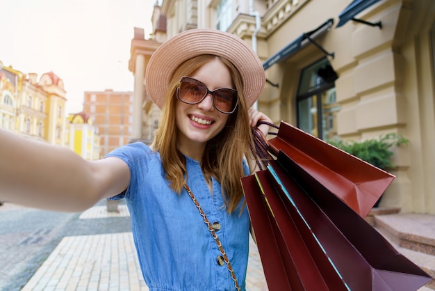 Jonge vrouw met boodschappentassen selfie wandelen in een stad op zomerdag maken