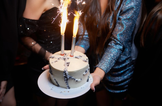 Jonge vrouw met bord met smakelijke verjaardagstaart tegen onscherpe lichten