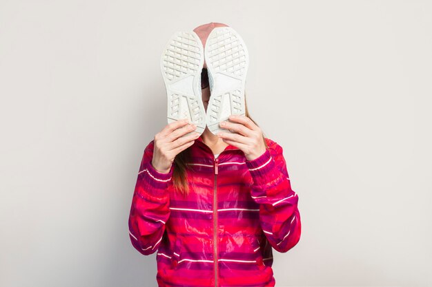 Jonge vrouw met bril, hoed en roze sportjasje met ernstig gezicht heeft betrekking op haar gezicht met sneakers