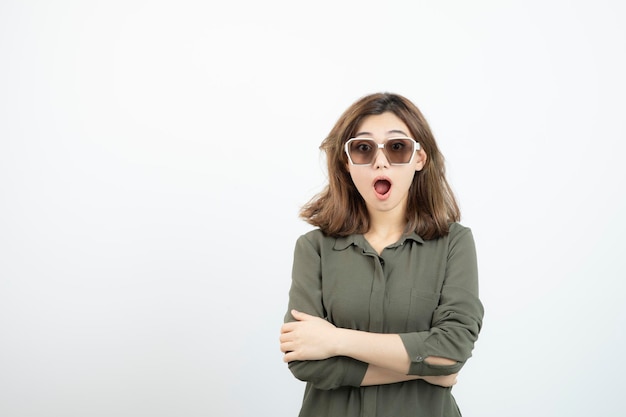 Jonge vrouw met bril permanent met verbaasde uitdrukking over witte muur. Hoge kwaliteit foto