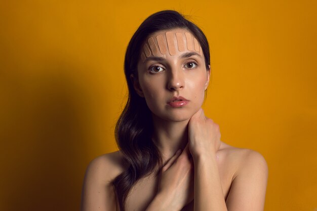 Jonge vrouw met bruine kinesiologietape op het geïsoleerde gezicht