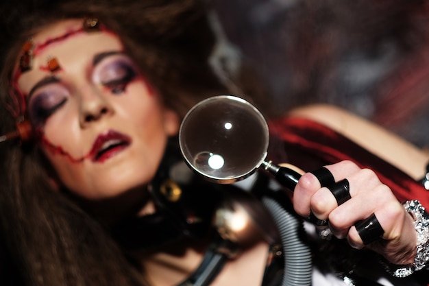 Jonge vrouw met creatieve make-up die een vergrootglas vasthoudt