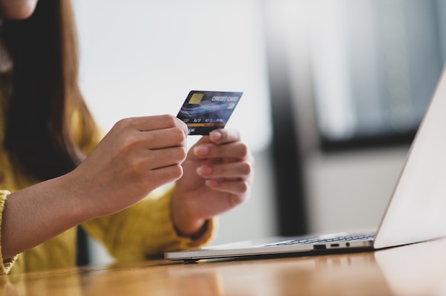 Jonge vrouw met creditcard in de hand en laptop op tafel, online winkelen, creditcardbetaling, close-up shot.