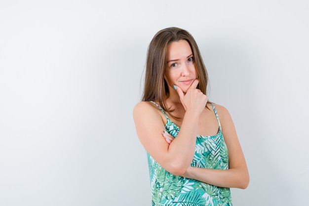 Jonge vrouw met de hand op de kin en zelfverzekerd, vooraanzicht.