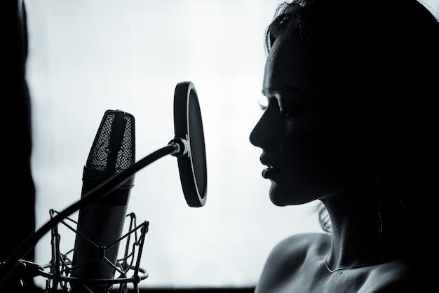 Jonge vrouw met de microfoon in de opnamestudio. Professionele vocale opname. Mooi meisje zanger. Portret. Detailopname.