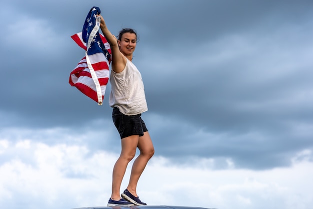 Jonge vrouw met de vlag van Amerika tegen de achtergrond van de hemel.