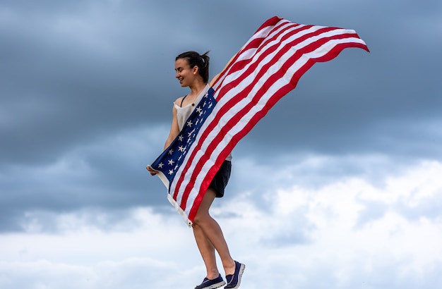 Jonge vrouw met de vlag van Amerika tegen de achtergrond van de hemel.