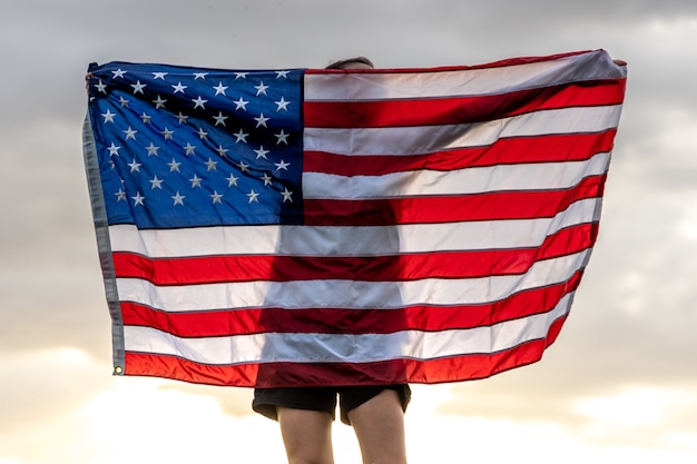 Jonge vrouw met de vlag van de Verenigde Staten genieten van zonsondergang in de natuur.