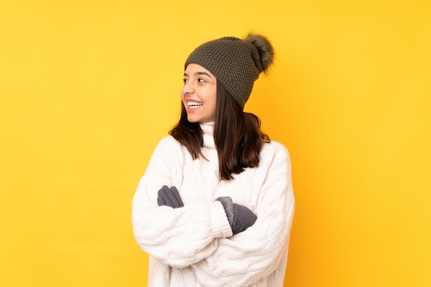 Jonge vrouw met de winterhoed over geïsoleerde gele gelukkig en glimlachende muur