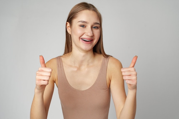 Jonge vrouw met duimen omhoog op een teken op een grijze achtergrond