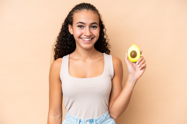 Jonge vrouw met een avocado geïsoleerd op een beige achtergrond die veel lacht