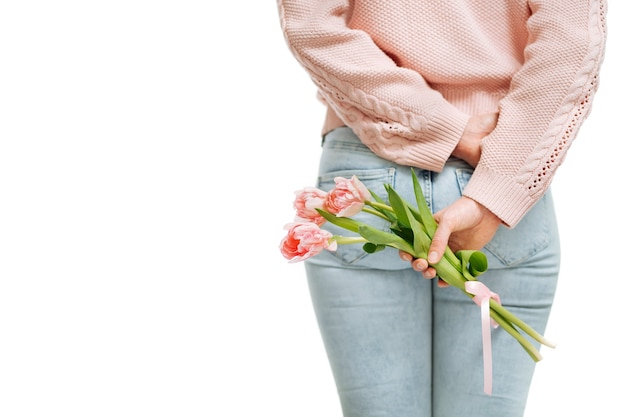 Jonge vrouw met een boeket roze tulpen achter haar rug op een witte achtergrond. Tekstruimte, selectieve focus.