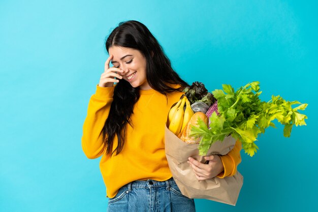 Jonge vrouw met een boodschappentas geïsoleerd op blauw lachen