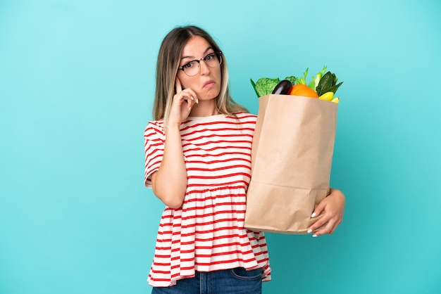 Jonge vrouw met een boodschappentas geïsoleerd op een blauwe achtergrond, denkend aan een idee