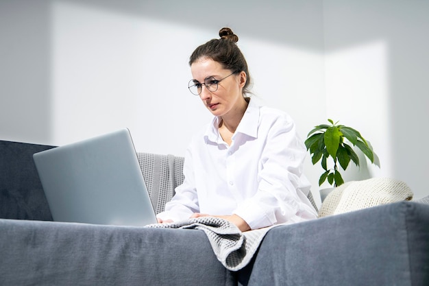 Jonge vrouw met een bril die op een laptop werkt terwijl ze op een bank zit