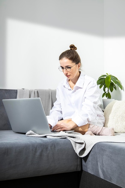 Jonge vrouw met een bril die op een laptop werkt terwijl ze op een bank zit