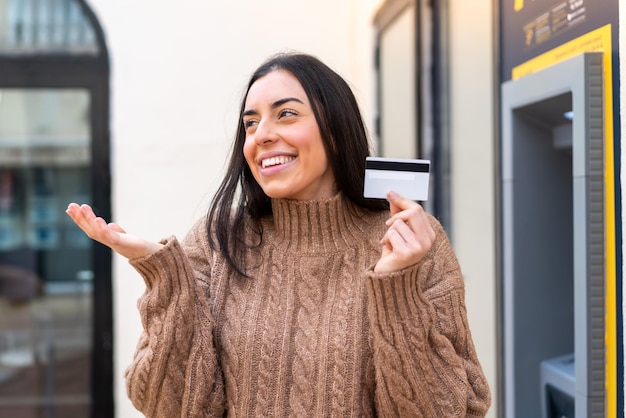 Jonge vrouw met een creditcard buitenshuis met een verrassende gezichtsuitdrukking