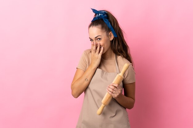 Jonge vrouw met een deegroller blij en glimlachend die mond bedekt met handen