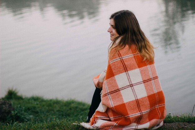 Jonge vrouw met een deken zit aan de oever van het meer
