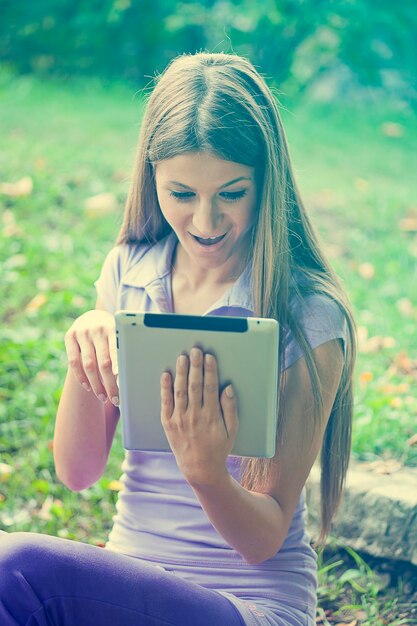 Jonge vrouw met een digitale tablet terwijl ze op het grasveld in het park zit