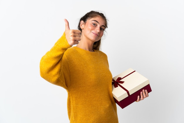 Jonge vrouw met een geschenk geïsoleerd op een witte muur met duimen omhoog omdat er iets goeds is gebeurd