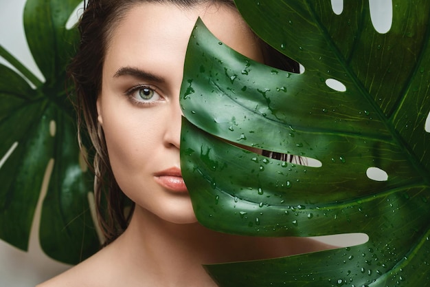 Jonge vrouw met een gladde huid die Monstera deliciosa plantenblad vasthoudt