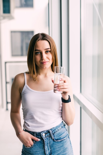 Jonge vrouw met een glas water zittend op de bank in de kamer