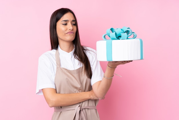 Jonge vrouw met een grote cake over geïsoleerde muur met droevige uitdrukking